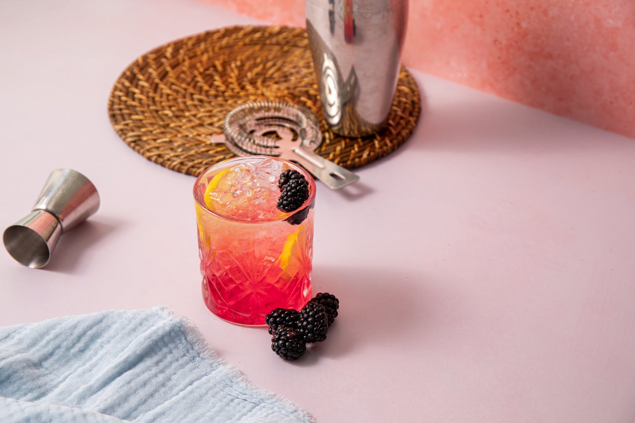 about-02 Colorful blackberry lemon cocktail with ice on a pink surface, perfect for summer gatherings.