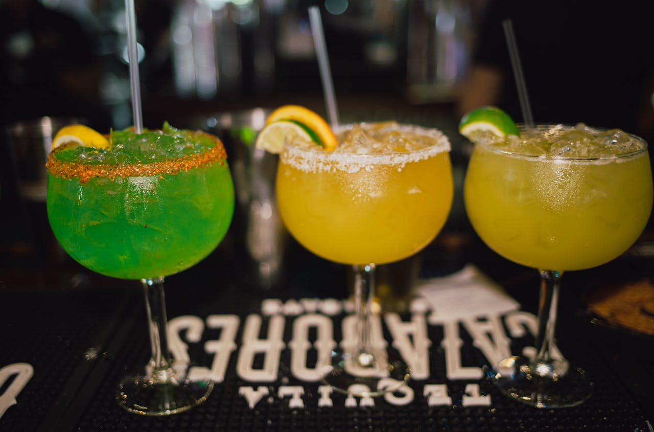 services-img Three colorful margaritas with citrus garnishes showcased in a lively bar setting.