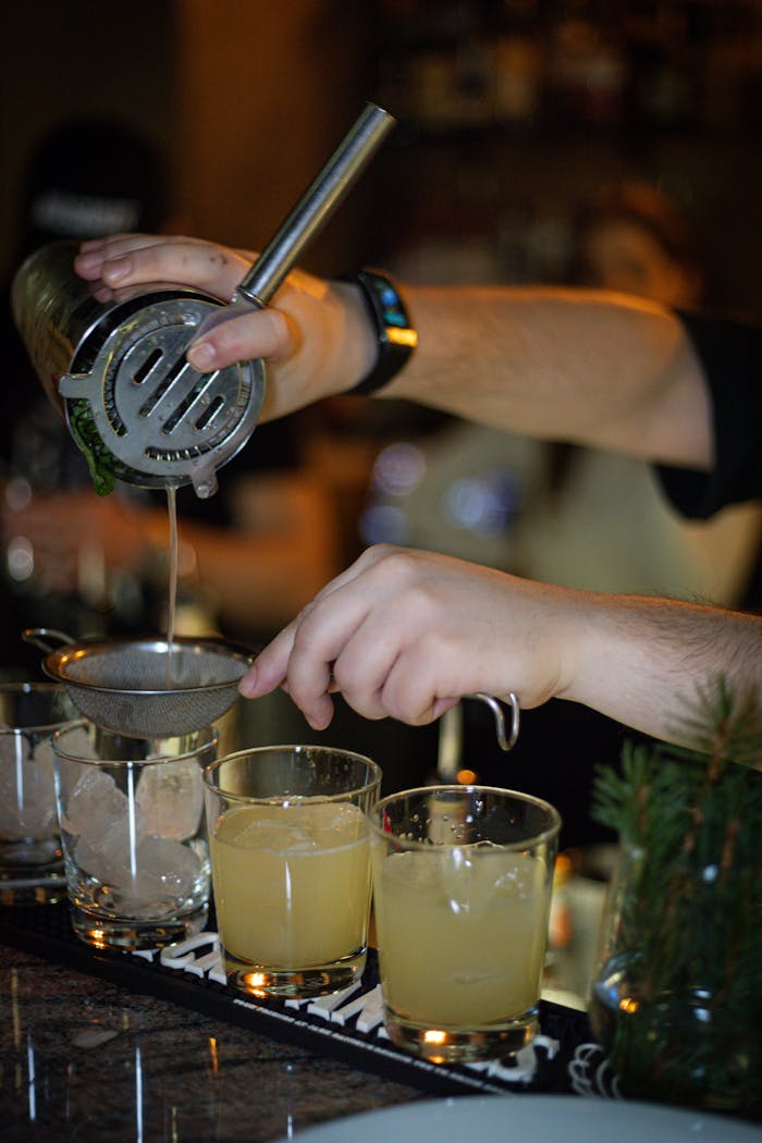 services-04 Bartender mixing citrus cocktails with a strainer at an indoor bar.